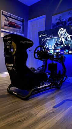 a gaming room with two monitors and a racing car on the floor in front of it