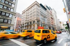 yellow taxi cabs are driving down the street in front of tall buildings and traffic lights