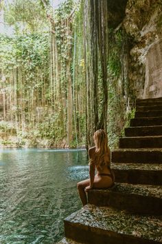 a woman sitting on some steps in front of a body of water surrounded by trees