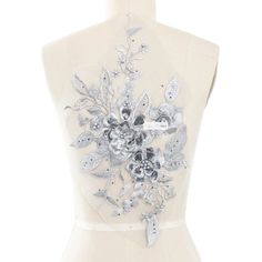 the back of a white dress with silver flowers and leaves on it's chest