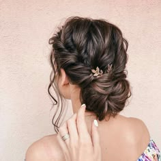 a woman with her hair in a low bun, wearing a flowered dress and holding her hand to her face