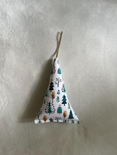 a small triangle shaped ornament with trees and animals on white fabric, hanging from a wooden stick