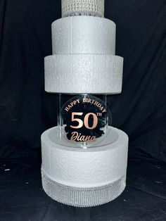 a three tiered cake sitting on top of a white tablecloth covered pedestal with a 50th birthday sign