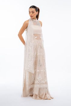 A long ivory organza shirt is delicately embellished with aari embroidery and tilla worked motifs, with a fringe trim accentuating the daaman. Featuring a pre tied bow on the collar, the shirt is paired with a matching charmeuse choli and draped skirt. Model Height is 5'5 and Shirt Length is 53' Embellished Embroidered Dress For Wedding, Elegant Semi-stitched Embellished Embroidered Dress, White Reception Dress For Transitional Season, Elegant Off White Festive Gown, Elegant Off-white Festive Gown, Elegant Off-white Festive Sets, Beige Party Sets With Traditional Drape, Embellished Embroidered Fabric For Wedding, Elegant Embellished Chanderi Lehenga