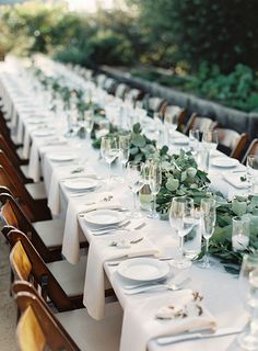 a long table is set with white plates and silverware