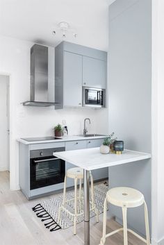 a kitchen with grey cabinets and white counter tops, two stools are in front of the sink