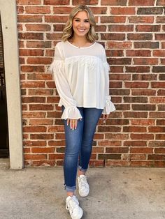 a woman standing in front of a brick wall with her hands on her hips and smiling