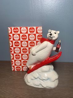 a white bear figurine on top of a red surfboard with a box in the background