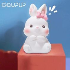 a small white rabbit figurine sitting on top of a red block with the word goup above it