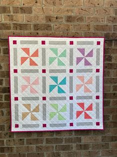 a quilted wall hanging on a brick wall next to a brick wall with an orange, green, pink and blue pinwheel design