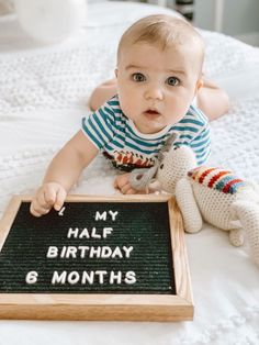 a baby laying on top of a bed next to a chalkboard with the words my half birthday 6 months