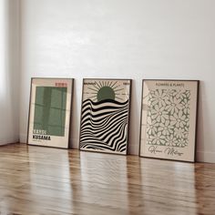 three framed art prints sitting on top of a hard wood floor next to a window