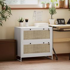 a white cabinet sitting next to a desk with a laptop on top of it and potted plants