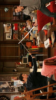 two people standing in a living room with bookshelves and other items on the shelves