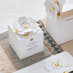 two white boxes with gold accents and flowers on the top one has a card in it