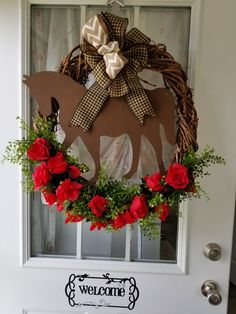 a welcome sign hanging on the front door with red roses and greenery around it