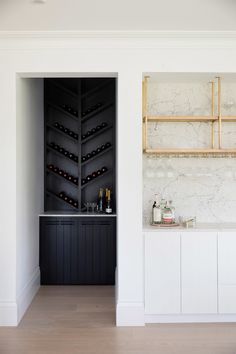 a kitchen with white cabinets and marble counter tops, wine rack in the back wall