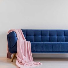 a blue couch with a pink blanket on it and a white wall in the background