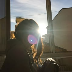 a woman sitting in front of a window with the sun shining through her eyes and behind her head