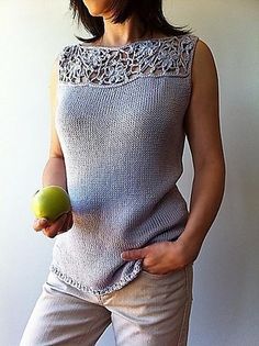 a woman holding an apple in her right hand and wearing a sleeveless sweater on