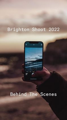 someone holding up their cell phone to take a photo with the ocean in the background