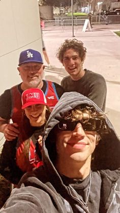 three men standing next to each other in front of a building with a baseball cap on