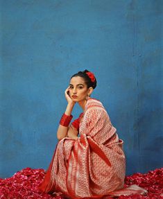 a woman sitting on the ground in a red and white sari with her hand to her face