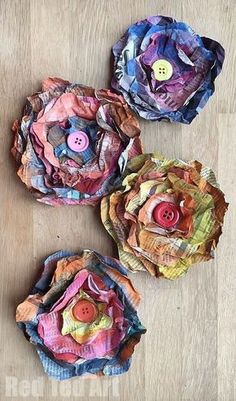 three paper flowers with buttons on them sitting on a wooden table next to each other