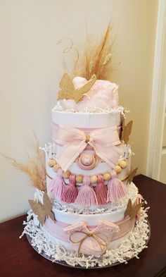 a three tiered cake with pink and gold decorations on it's sides, sitting on top of a wooden table