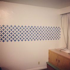 the wall is painted with blue and white geometric designs, along with a wooden dresser