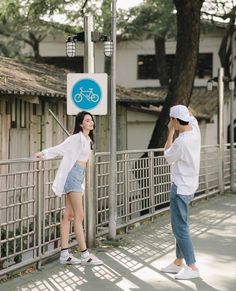 two people standing next to each other near a fence with a bicycle sign on it