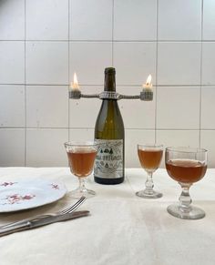 two glasses and a bottle sitting on a table next to a plate with silverware