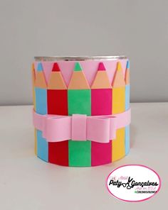 a paper crown made out of colored pencils on a white surface with a pink ribbon around it