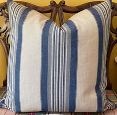 a blue and white striped pillow sitting on top of a wooden chair next to a yellow wall