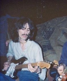 two men sitting next to each other with guitars in their hands and one man playing the guitar