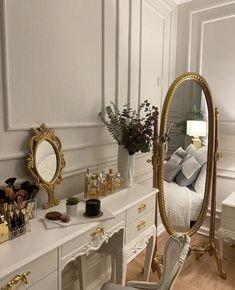 a bedroom with white furniture and gold accents on the walls, along with a large mirror