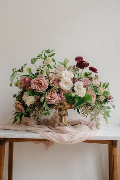 an arrangement of flowers on a table with a pink blanket and wooden chair in the background