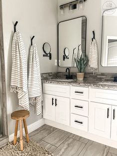 a bathroom with white cabinets and marble counter tops, two mirrors above the sink and one stool in front of it