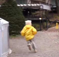 a young child wearing a yellow jacket running down a path in front of a building