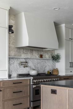 a kitchen with white cabinets and marble counter tops, an oven hood over the stove