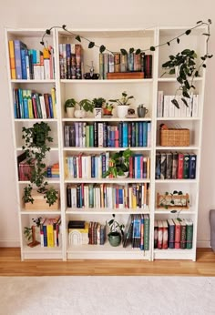 a bookshelf filled with lots of books and plants on top of white shelves