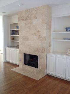 a living room with white cabinets and a fireplace in the center, built in bookshelves