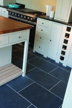 a kitchen with black slate flooring and white cabinets, an island countertop and drawers