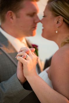 a bride and groom holding each other's wedding ring as the sun sets behind them