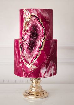 a pink and gold cake on top of a metal stand with marbled icing