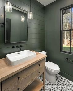 a white toilet sitting next to a bathroom sink under a mirror on top of a wooden counter