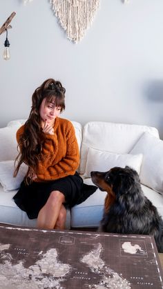 a woman sitting on top of a white couch next to a black and brown dog