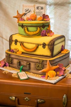 a cake that is sitting on top of a piece of brown luggage with shells and seashells around it