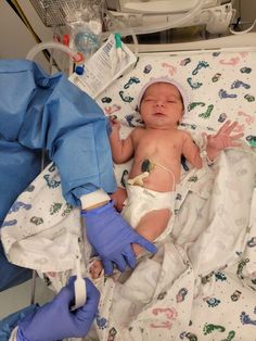 a baby laying on top of a hospital bed next to an iv drip and gloves