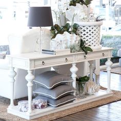 a white table topped with lots of pillows and vases filled with flowers next to a lamp